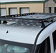 A Large Black Revrack tray atop a newer style White Van, parked near enclosed storage units
