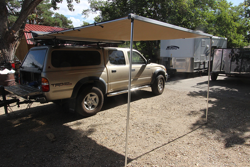 8 foot wide weather awning attached to a medium Revrack Tray, atop a two thousand four gold toyota tacoma pickup truck with a gold topper
