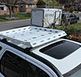 Small white revrack tray atop a white two thousand four honda crv with en enclosed white trailer in the neighborhood background