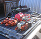 three orange and white chainsaws and red fuel cans in a revrack tray atop a gold nissan pathfinder
