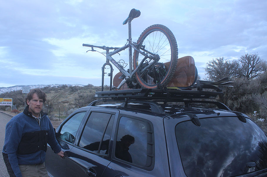 a revrack user stands next to the driverside door of a two thousand five hun die with a revrack carrying bikes and skis on top