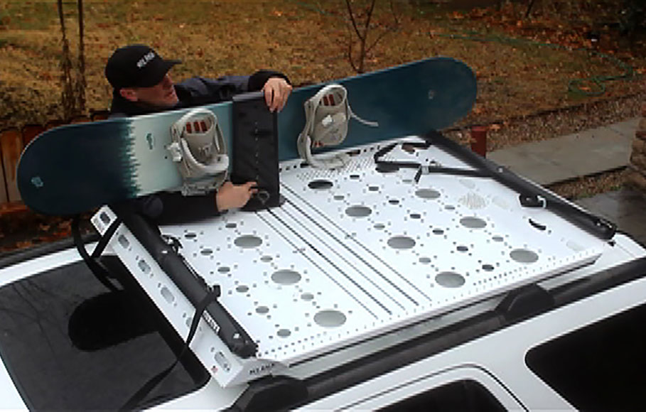 looking down at a man in a black baseball hat and jacket attaches two snowboards to a small revrack using the sliding revrack